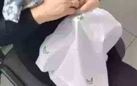 Pani z rudymi włosami w czarnej bluzce i czarnych spodniach z szalikiem zarzuconym na szyi w kolorze niebiesko beżowym siedzi na krześle i trzyma w ręce białą poszewkę, na kt&oacute;rej wyszywa zielona nitką wcześniej odrysowany wz&oacute;r. W tle widać okno z zawieszo